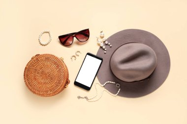 Bej arka planda cep telefonu, küpe ve güneş gözlüğü olan şık aksesuarlar. Üst görünüm
