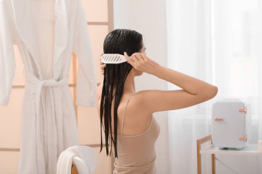 Güzel genç bir kadın banyoda saçını maskeyle tarıyor.