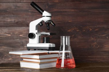 Modern mikroskop ile kimyasal matara ve masa üzerinde ahşap arka plan karşı kitaplar