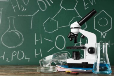 Modern mikroskop, petri kabı ve matara tahtada kimyasal formüllerle birlikte.