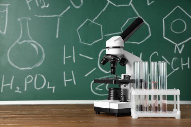 Modern mikroskop ve mataralar ahşap masada, kimyasal formüllerle birlikte.