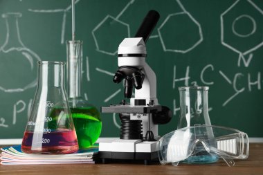 Modern mikroskop, koruyucu gözlükler ve kimyasal formüllü tahta masanın yanındaki mataralar.