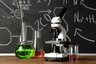 Modern mikroskop ve mataralar ahşap masada, kimyasal formüllerle birlikte.