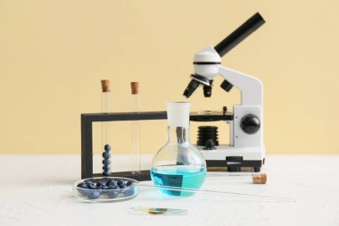 Sarı duvarın yanındaki masada mikroskop ve böğürtlenli profesyonel laboratuvar bardakları.
