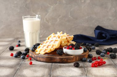 Lezzetli Belçika waffleları, güvertede böğürtlen ve masada gri arka planda bir bardak süt.