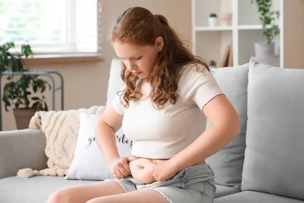 stock image Young woman in tight shorts sitting on sofa at home. Weight gain concept