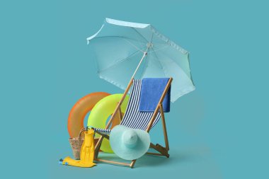 Güverte sandalyesi, plaj şemsiyesi, hasır çanta, şapka, palet, havlu ve mavi arka planda şişirilebilir halkalar.