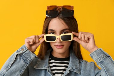 Sarı arka planda farklı stil güneş gözlüklü güzel bir genç kadın.