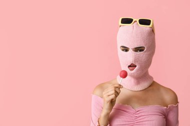 Güneş gözlüklü, kar maskeli güzel bir kadın ve pembe arka planda tatlı bir lolipop.