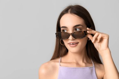 Gri arka planda şık güneş gözlüklü güzel bir kadın.