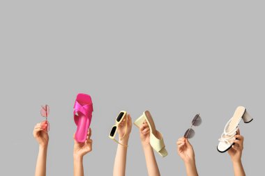 Şık güneş gözlüklü kadın elleri ve gri arka planda farklı sandaletler.