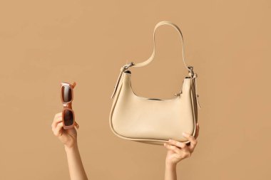 Şık güneş gözlüklü ve kahverengi çantalı kadın elleri.