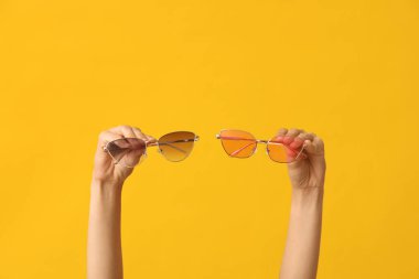 Female hands with different stylish sunglasses on yellow background