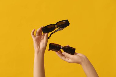 Female hands with different stylish sunglasses on yellow background