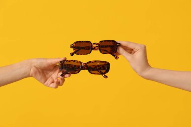 Sarı arka planda leopar desenli güneş gözlüğü takan kadın eller.