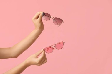 Female hands with different stylish sunglasses on pink background