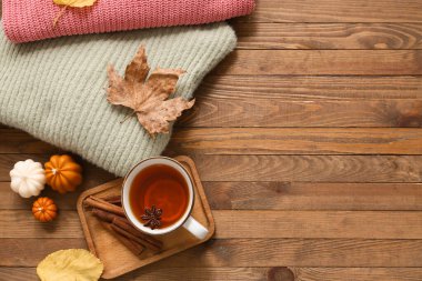 Bir fincan çay, sıcak süveterler ve ahşap arka planda mumlarla kompozisyon.