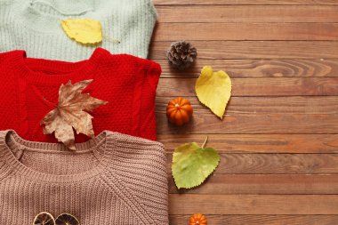 Şık kadın kazakları, mum ve sonbahar yapraklarıyla ahşap arka planda kompozisyon