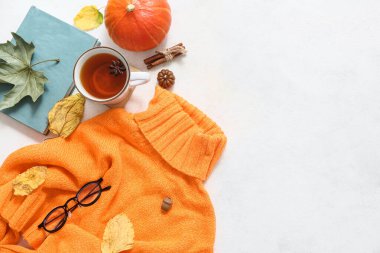 Süslü, sıcak süveter, kitap, bir fincan çay ve arka planda sonbahar dekoru olan kompozisyon