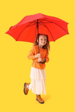 Sonbahar kıyafetleri içinde, sarı arka planda şemsiyesi olan şirin, mutlu bir kız.