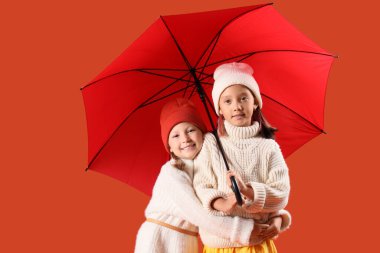 Sonbahar kıyafetleri içinde, turuncu arka planda şemsiyesi olan şirin küçük mutlu kızlar.