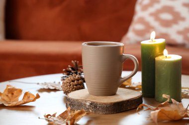 Bir fincan çay, yanan mumlar ve sonbahar yaprakları oturma odasında, yakın çekim.