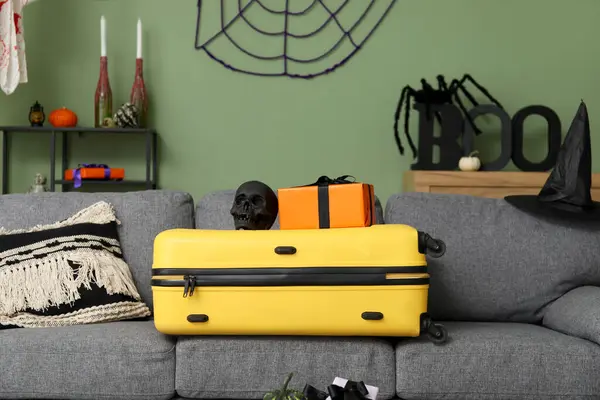 stock image Suitcase with skull and gift on sofa in living room decorated for Halloween