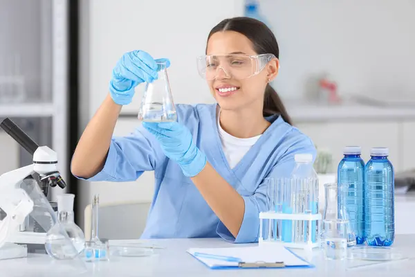 stock image Happy female young scientist with professional glassware examining water quality in research laboratory