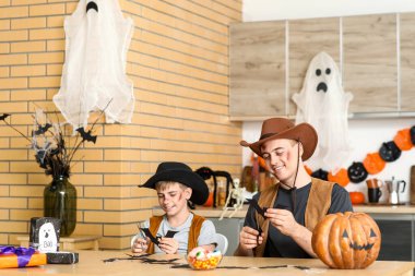 Baba ve oğlu Cadılar Bayramı için giyinmiş kovboylar gibi mutfakta kağıt yarasalar kesiyorlar.