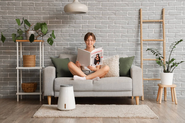 Молодая женщина с увлажнителем воздуха читает журнал на диване дома