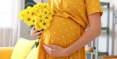 Evde kasımpatı çiçekli hamile bir kadın, yakın plan.