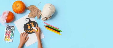 Çocukların elleri Cadılar Bayramı kutlamaları için mavi arka planda süslemeler yapıyor ve metin için yer var.