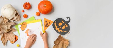 Çocukların elleri, cadılar bayramı için gri arka planda şenlik süslemeleri yapıyor ve metin için yer var.