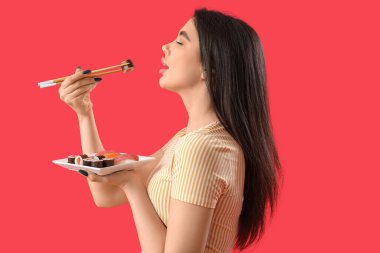 Kırmızı arka planda suşi yiyen genç bir kadın.