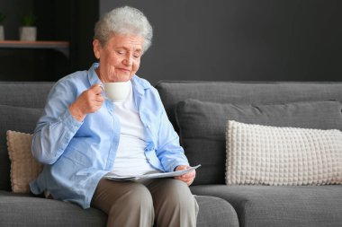 Evde elinde bir fincan kahveyle gazete okuyan yaşlı bir kadın.