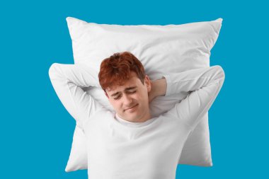 Young man with soft pillow on blue background