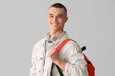 Gri arka planda sırt çantası ve kulaklığı olan bir erkek öğrenci.