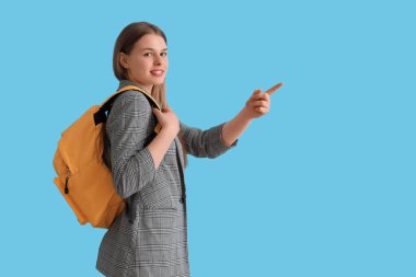 Sırt çantalı kız öğrenci mavi arka plandaki bir şeyi işaret ediyor.
