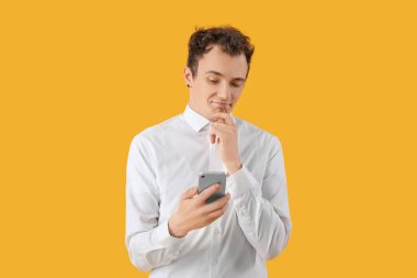 Sarı arka planda akıllı telefonu olan düşünceli bir genç adam.