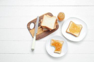 Lezzetli tost tabakları, kayısı reçeli ve beyaz ahşap arka planda bıçak.