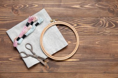 Kahverengi ahşap zemin üzerinde küflü iplikler, makas ve tuval ile ahşap işlemeli çember.