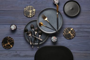 Temiz tabaklar, çatal bıçak takımı ve mavi ahşap masada bardak altlığı.