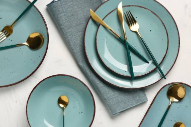 Masa seti, temiz tabaklar, altın çatal bıçak ve beyaz arka planda peçete.