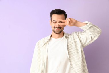 Leylak arka planında zafer jesti gösteren yakışıklı bir adam.