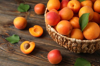 Tahta arka planda taze kayısılarla dolu sepet.