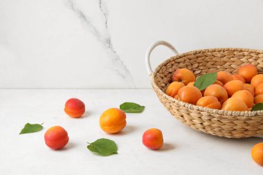 Beyaz masada taze kayısılarla dolu hasır sepet.