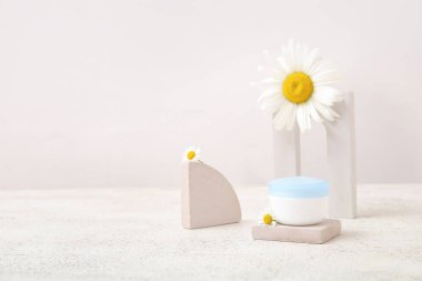 Hafif arkaplanda kozmetik ürün kavanozu, sıva podyumları ve papatya çiçekleri kompozisyonu