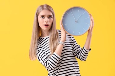 Sarı arka planda saati olan stresli genç bir kadın. Son teslim tarihi kavramı