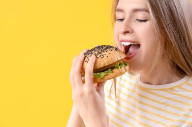 Sarı arka planda lezzetli burger yiyen genç bir kadın, yakın plan.