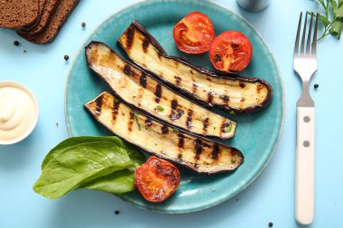 Açık mavi arka planda leziz ızgara patlıcan ve domates tabağı.